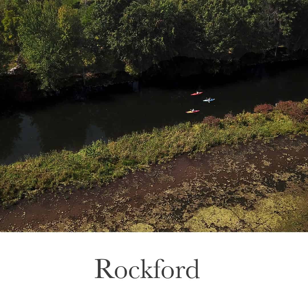 Kayakers on the river in downtown Rockford, Michigan, highlighting the scenic waterfront lifestyle near local homes and properties.